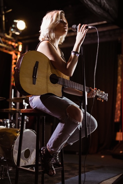 Female performer singing while holding guitar on stage at nightclub